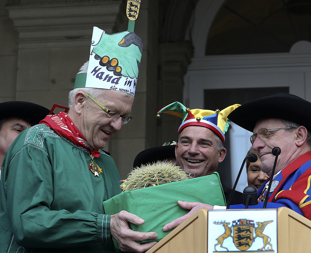 Ministerpräsident Winfried Kretschmann (l.) erhält von den Narren einen Hut und einen Kaktus.
