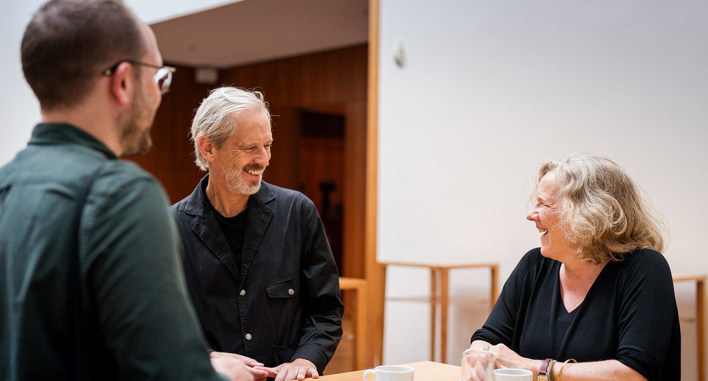 Alistair Hudson und Helga Huskamp, ZKM unterhalten sich. Sie stehen an einem Bistrotisch aus hellem Holz. 