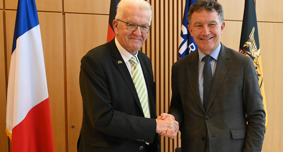 Ministerpräsident Winfried Kretschmann (links) und Franck Leroy (rechts), Präsident der Region Grand Est, stehen vor Fahnen und geben sich die Hand.