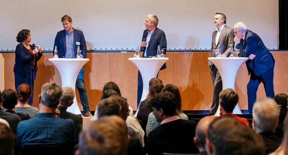 Podiumsdiskussion mit fünf Personen vor den Teilnehmenden im Saal.