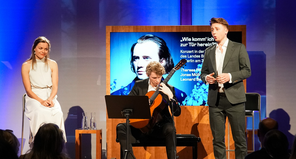 Alumni der Liedakademie: Theresa Pilsl und Jonas Müller mit Gitarrist Leonard Becker auf der Bühne im Großen Saal der Landesvertretung.