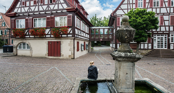 Symbolbild: Eine Frau sitzt an einem Dorfbrunnen. (Foto: © dpa)