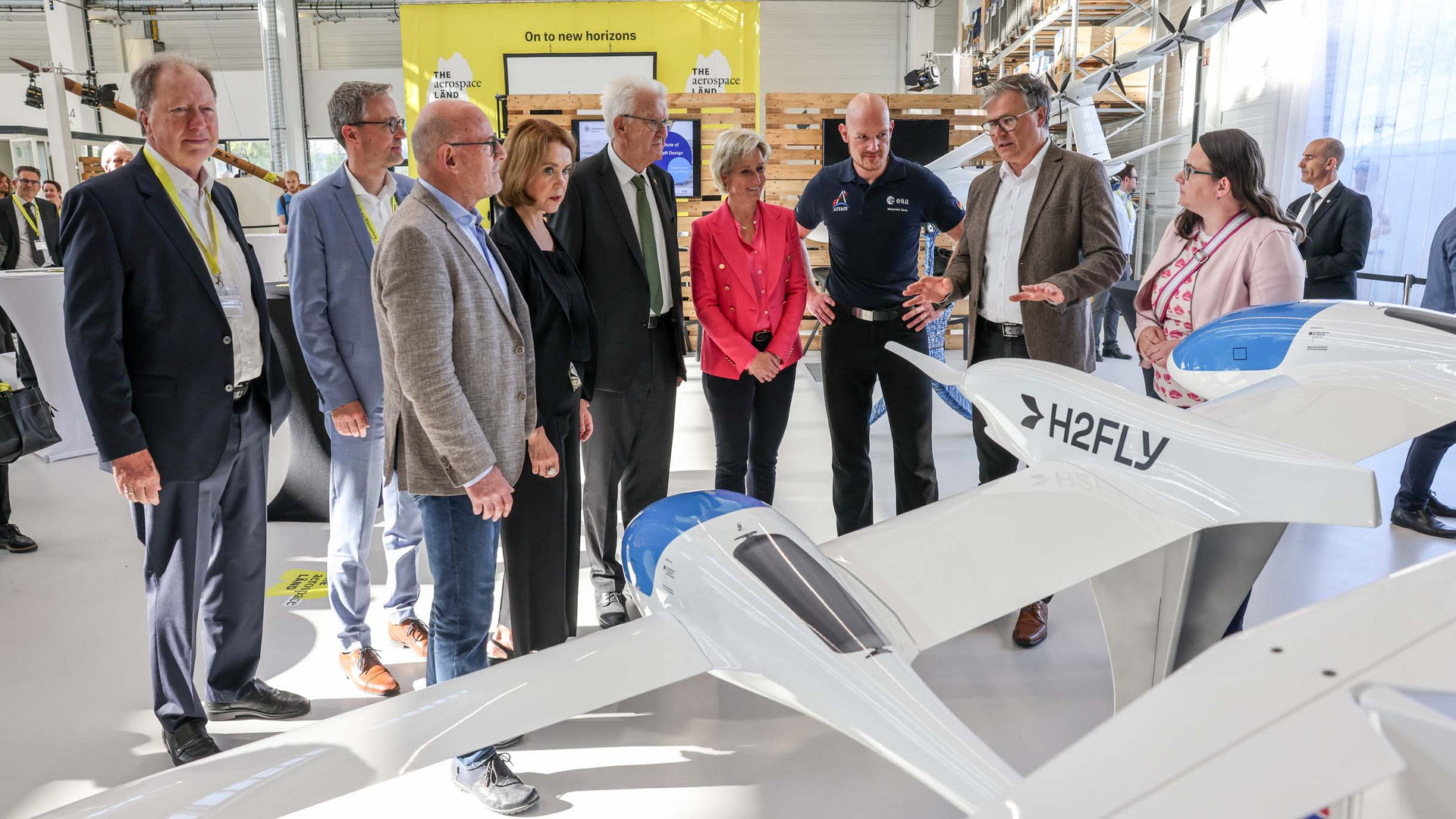 Ministerpräsident Winfried Kretschmann und weitere Teilnehmende stehen bei einem Rundgang an einem Modell des Forschungs- und Versuchsflugzeugs HY4.