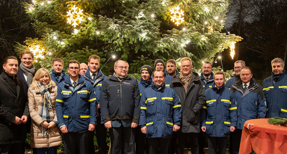 Gruppenfoto des THW-Teams mit Staatssekretär Rudi Hoogvliet, Yannick Bury MdB und Martin Aßmuth, Bürgermeister Hofstetten vor dem erleuchteten Weihnachtsbaum