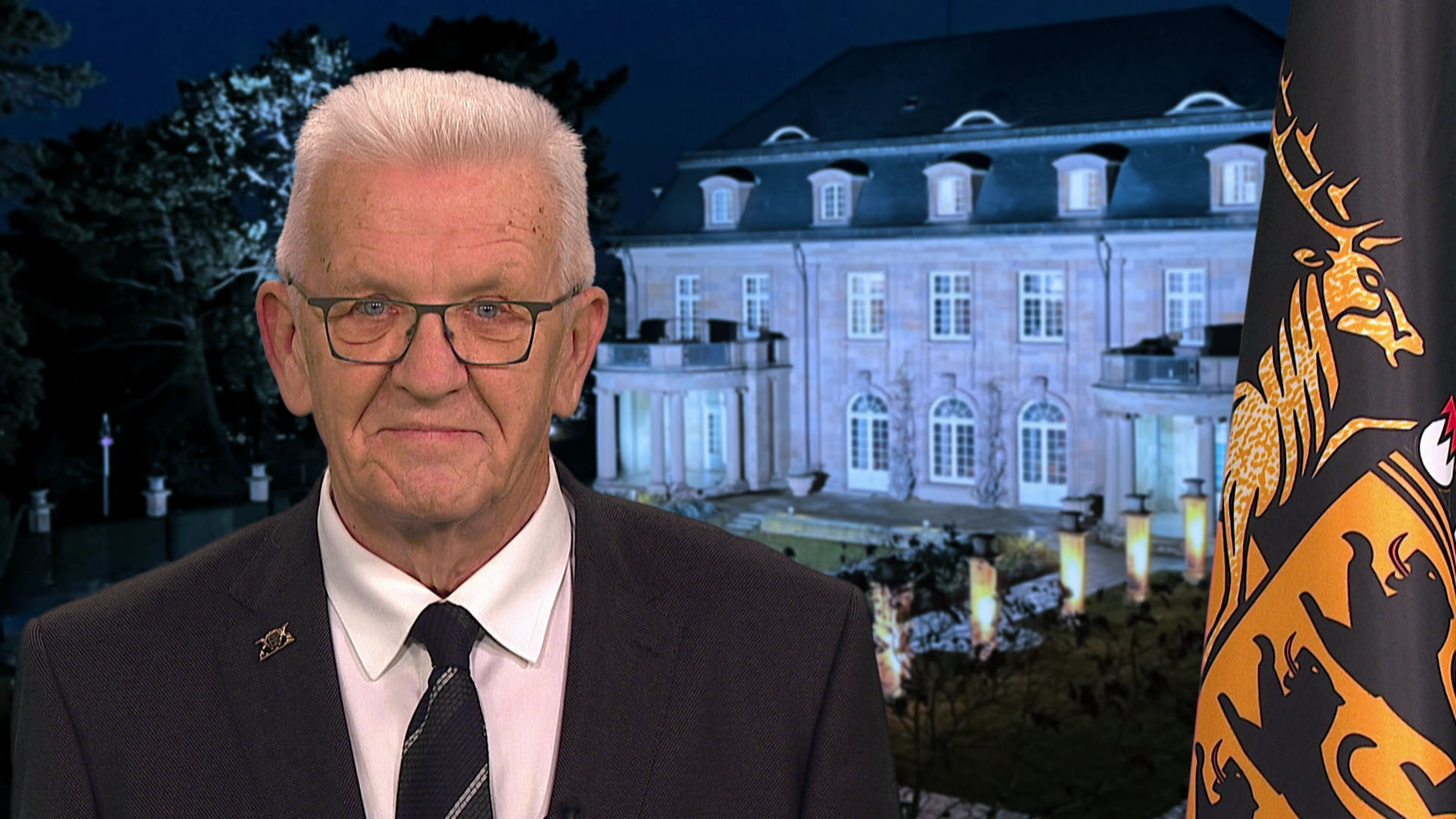 Ministerpräsident Winfried Kretschmann bei seiner Ansprache zum Jahreswechsel 2025/2026, im Hintergrund die Villa Reitzenstein, rechts im Bild die Baden-Württemberg-Fahne.