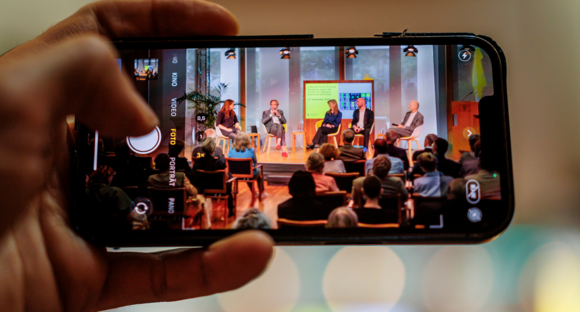 Durch ein Handy sieht man v.l.n.r.: Saskia Trebing, Prof. Dr. Claus Pias, Margit Rosen, Harm van den Dorpel, Dr. Wolfgang Ullrich