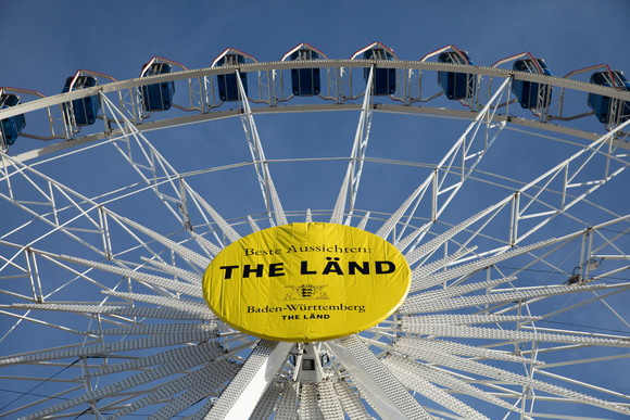 Riesenrad auf dem Stuttgarter Schlossplatz mit der Aufschrift „Beste Aussichten: THE LÄND“ und dem Landeswappen