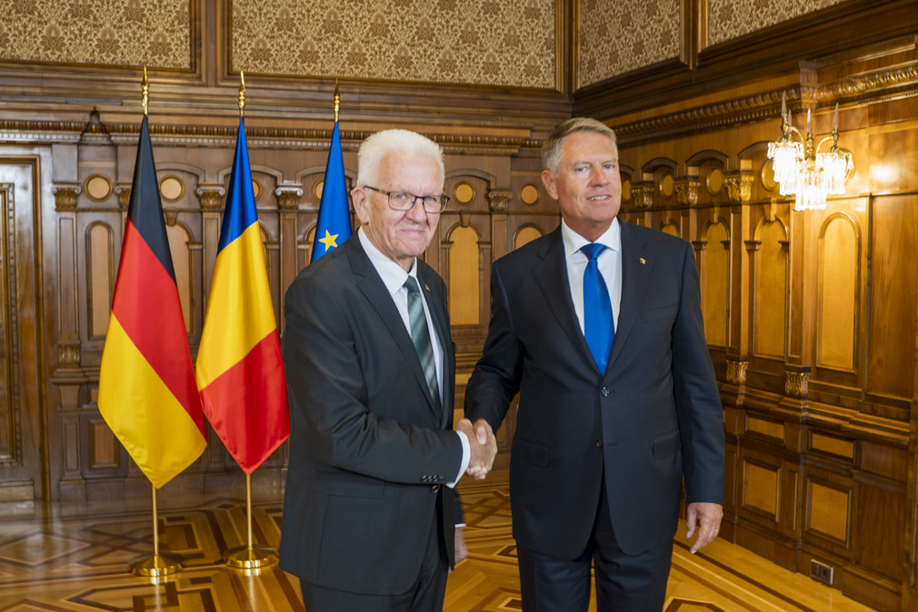 Ministerpräsident Winfried Kretschmann (links) und Rumäniens Staatspräsident Klaus Iohannis (rechts) stehen vor Fahnen und geben sich die Hand.