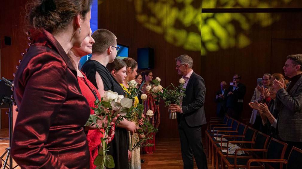 Staatssekretär Rudi Hoogvliet bedankt sich bei den Musikerinnen des Solidaritätskonzertes und überreicht weiße Rosen
