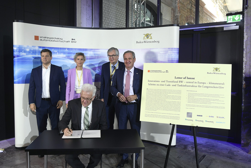 Ministerpräsident Winfried Kretschmann (vorne) unterzeichnet eine Absichtserklärung für ein „Pilot-Lade- und Wasserstoff-Tankinfrastrukturprojekt für Langstrecken-Lkw“.