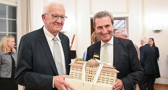 Ministerpräsident Winfried Kretschmann (links) überreicht dem ehemaligen Ministerpräsidenten Günther Oettinger (rechts) bei einem Empfang anlässlich dessen 70. Geburtstages ein Bienenhotel in Form der Villa Reitzenstein.