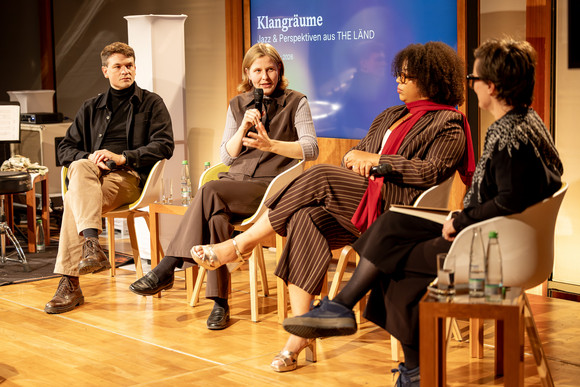 Die Diskussionsrunde von links nach rechts im Halbkreis auf Stühlen neben den Instrumenten auf der Bühne: Janning Trumann, Tabea Kind, Gabriele Maurer, Moderatorin Julia Neupert