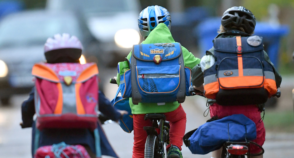 Kinder sind auf einer Straße mit dem Fahrrad unterwegs zur Schule. (Foto: © dpa)
