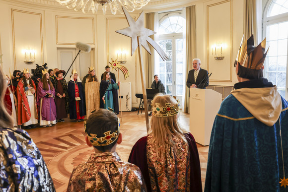 Ministerpräsident Winfried Kretschmann (hinten rechts) spricht zu den Sternsingerinnen und Sternsingern.