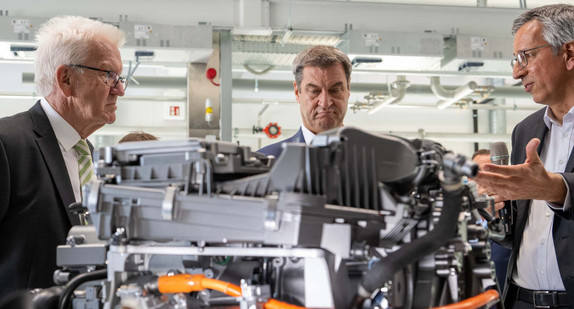 Die Ministerpräsidenten Winfried Kretschmann (links) und Markus Söder (Mitte) lassen sich im Zentrum für Sonnenenergie- und Wasserstoff-Forschung Baden-Württemberg in Ulm von Vorstandsmitglied Markus Hölzle (rechts) ein Brennstoffzellensystem für Fahrzeugantriebe erklären.