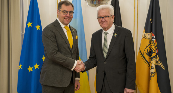 Ministerpräsident Winfried Kretschmann (r.) und der ukrainische Botschafter Oleksii Makeiev (l.) stehen in der Villa Reitzenstein vor Fahnen und geben sich die Hand.