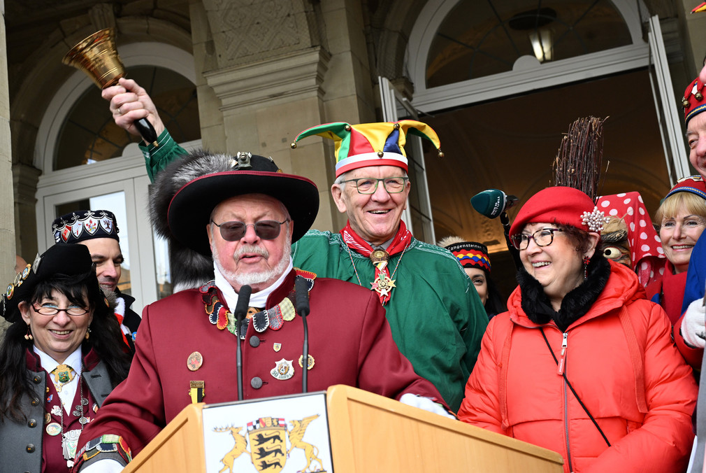 Ministerpräsident Winfried Kretschmann (Mitte) mit einer Glocke in der Hand, daneben stehen seine Frau Gerlinde sowie Närrinnen und Narren.