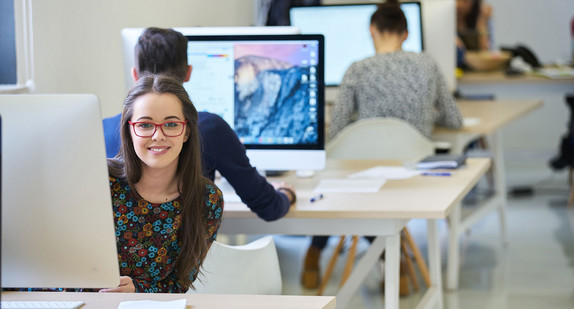 Eine junge Frau sitzt an einem Computer in einem Büro.