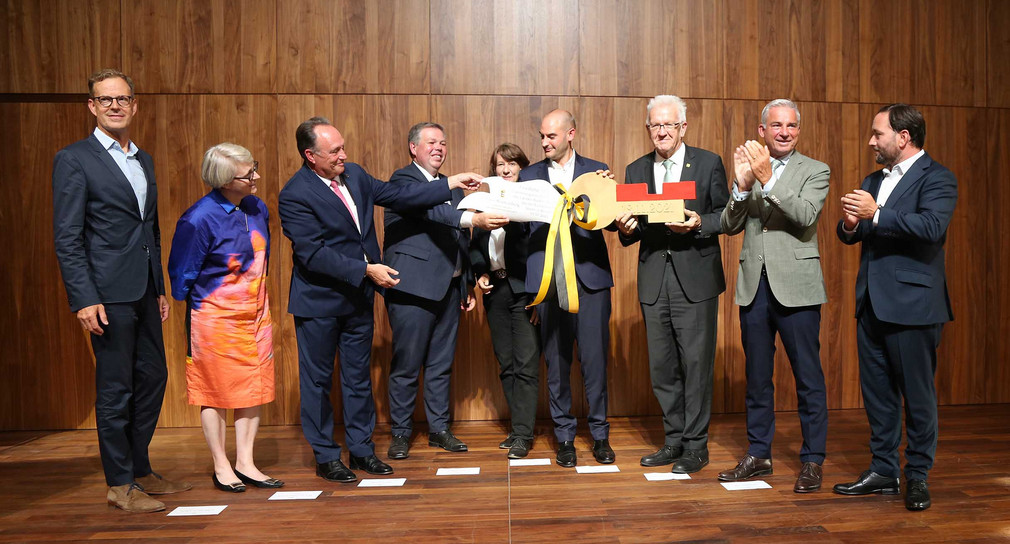 Gruppenbild auf der Bühne: Symbolische Schlüsselübergabe durch Ministerpräsident Winfried Kretschmann 