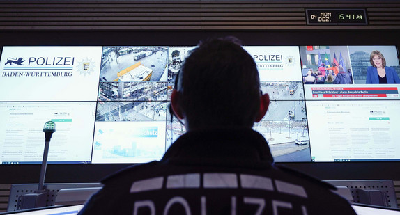 Ein Beamter steht im Führungs- und Lagezentrum des Polizeipräsidiums Mannheim vor einer Wand mit Bildschirmen.
