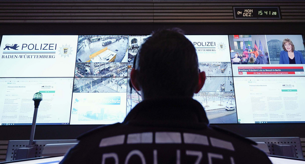 Ein Beamter steht im Führungs- und Lagezentrum des Polizeipräsidiums Mannheim vor einer Wand mit Bildschirmen.