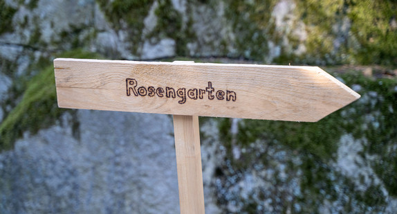 Ein Holzschild zeigt den Weg zum Rosengarten im Park der Villa Reitzenstein.