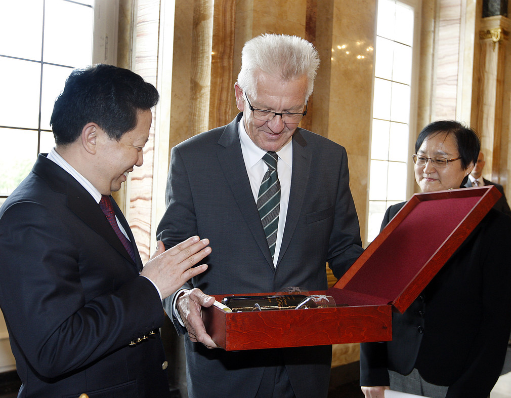 Ministerpräsident Winfried Kretschmann (M.) überreicht Gouverneur Qiufa Chen (l.) eine Weinbox.