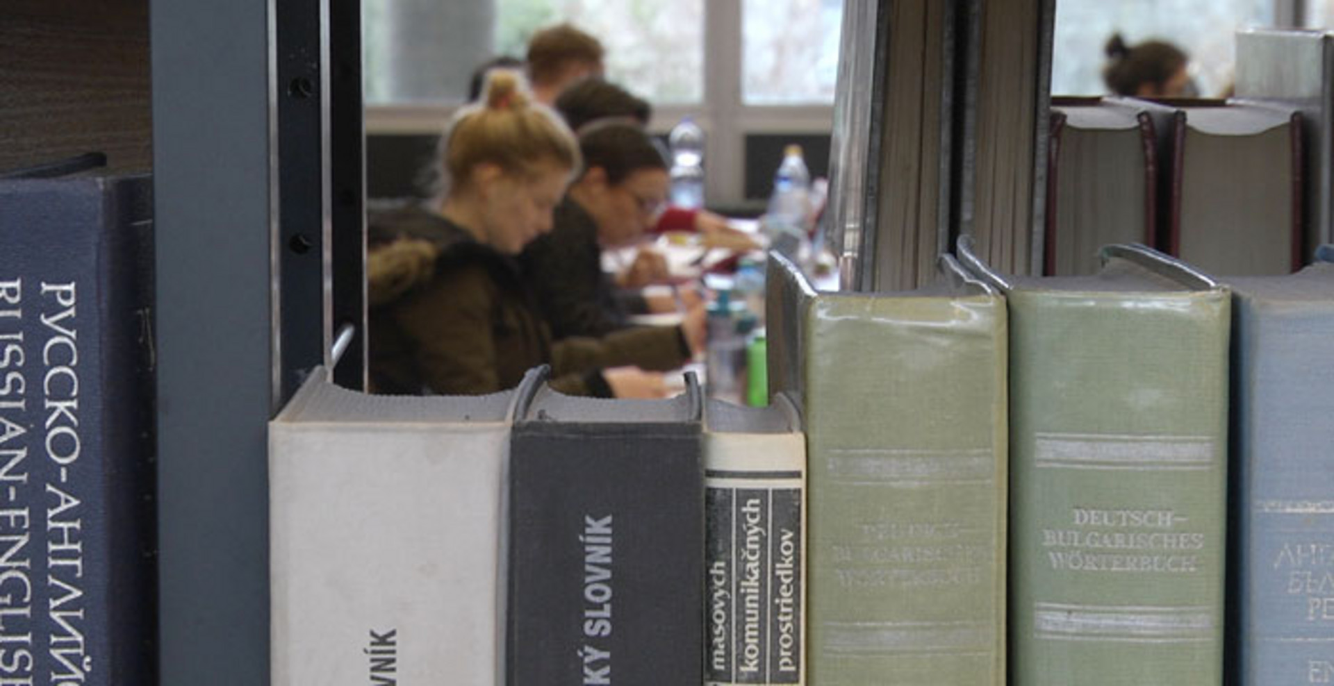 Studierende sitzen in einer Universitätsbibliothek und arbeiten.