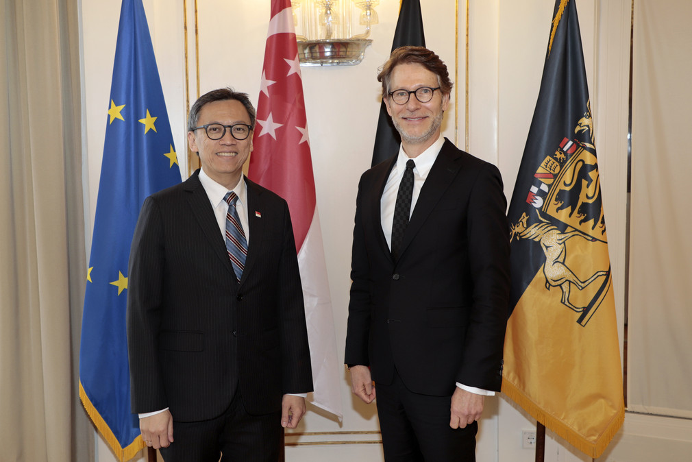 Staatsminister Dr. Florian Stegmann (rechts) und der Botschafter der Republik Singapur, Lee Chong Hock (links) stehen vor Fahnen.
