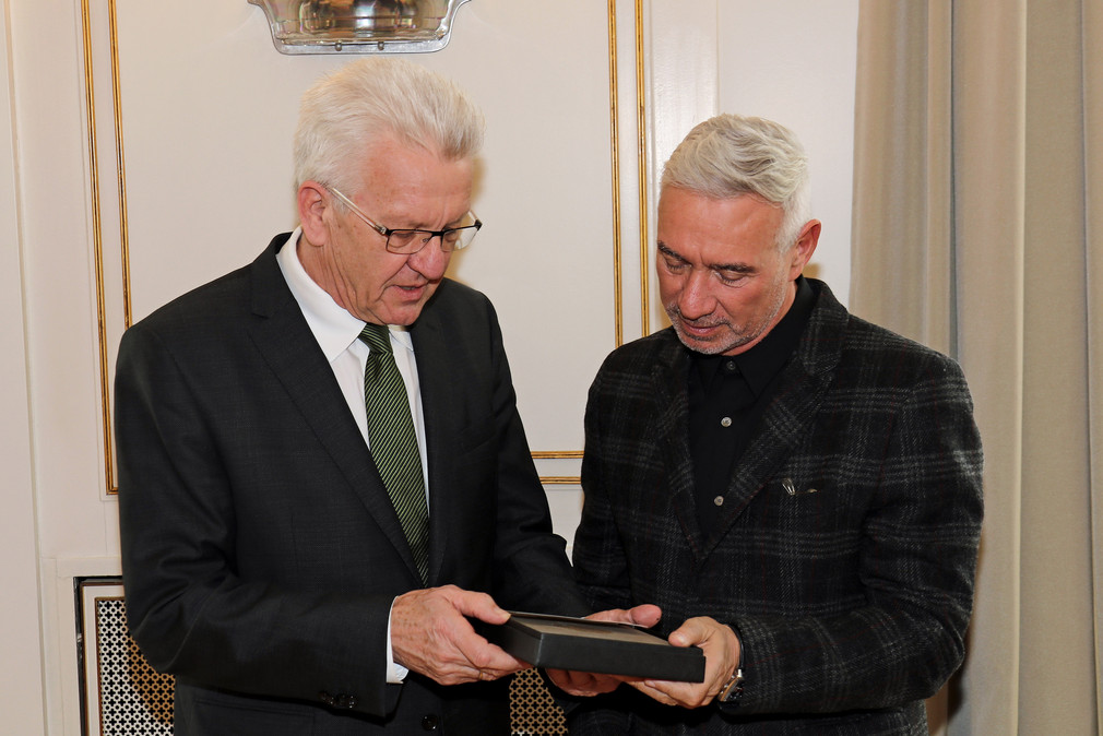 Ministerpräsident Winfried Kretschmann (l.) überreicht Roland Emmerich (r.) als Gastgeschenk einen Ammoniten aus Holzmaden.