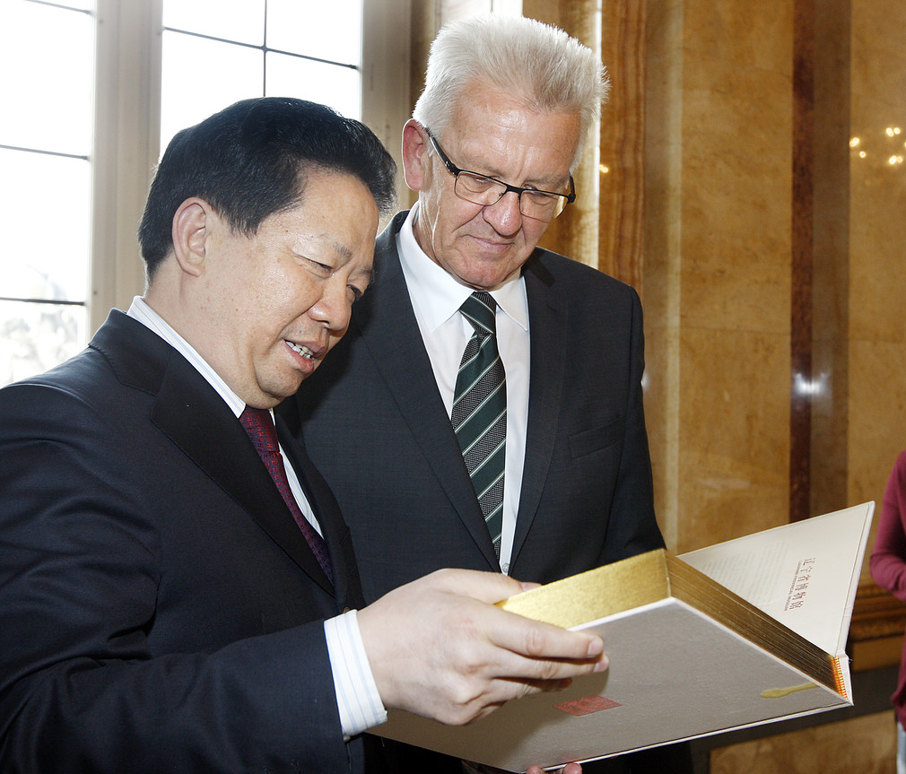 Gouverneur Qiufa Chen (l.) und Ministerpräsident Winfried Kretschmann (r.) sehen sich ein Buch, ein Gastgeschenk des Gouverneurs, an.