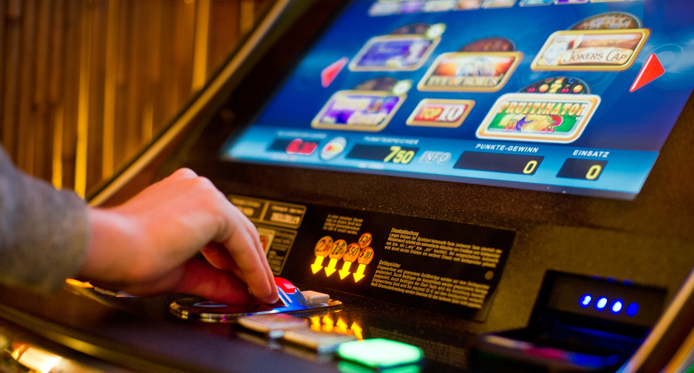 Eine Hand wirft Geld in einen Spielautomaten in einer Spielhalle.