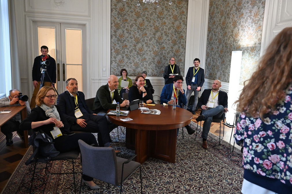 Eine Gruppe von Personen mit Kultusministerin Theresa Schopper (Mitte) sitzt an einem Tisch und verfolgt eine Präsentation.