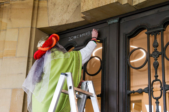 Eine Sternsingerin bringt an der Eingangstür der Villa Reitzenstein den Sternsinger-Segen an.