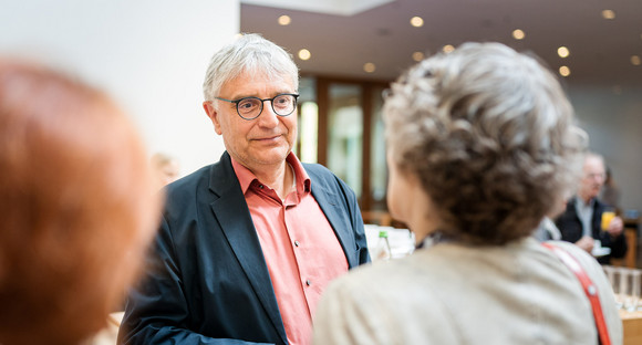 Staatssekretär Arne Braun im Gespräch mit Gästen. Herr Braun trägt ein rotes Hemd und ein graues Sakko. Seine Gesprächpartner sieht man nur schemenhaft.