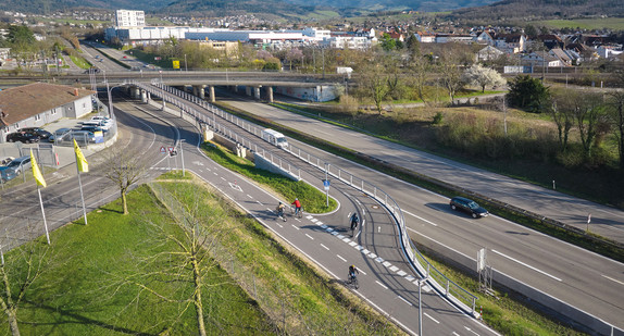 Ein breiter Radweg führt getrennt an einer Straße entlang und geht in eine Brücke über.