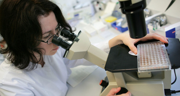 In einem ärztlichen Labor untersucht eine Frau eine Probe am Mikroskop.
