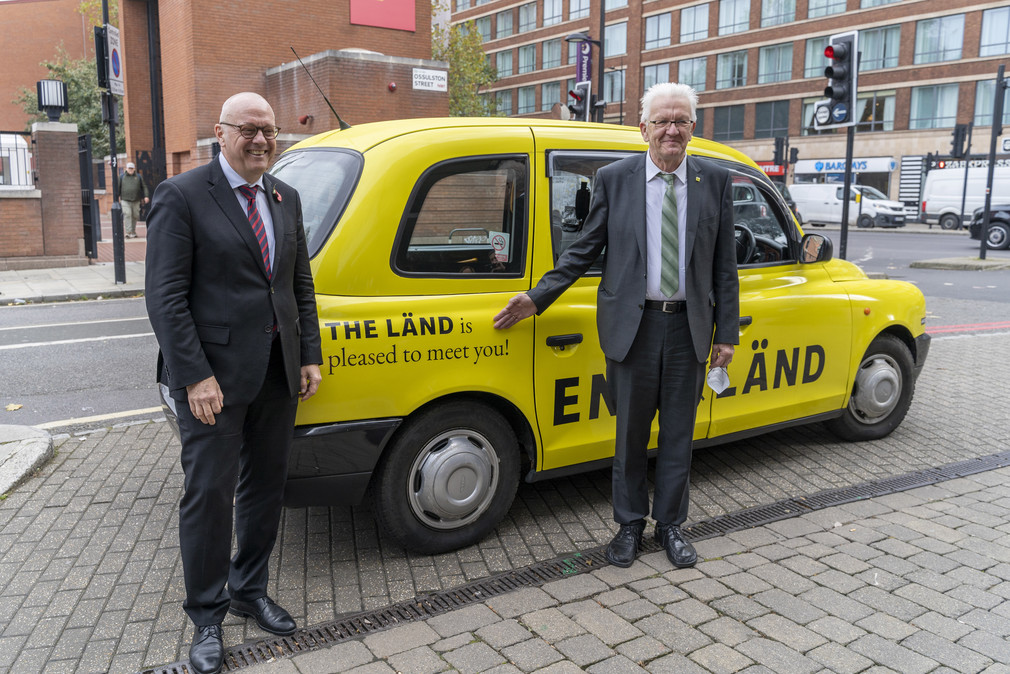 Andreas Michaelis (links), Botschafter der Bundesrepublik Deutschland im Vereinigten Königreich, und Ministerpräsident Winfried Kretschmann (rechts) vor einem Londoner Taxi im Design der neuen „THE LÄND“-Kampagne