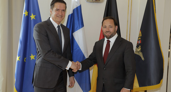 Staatssekretär Florian Hassler (rechts) und der finnische Botschafter Kai Jürgen Mikael Sauer (links) stehen vor Fahnen.