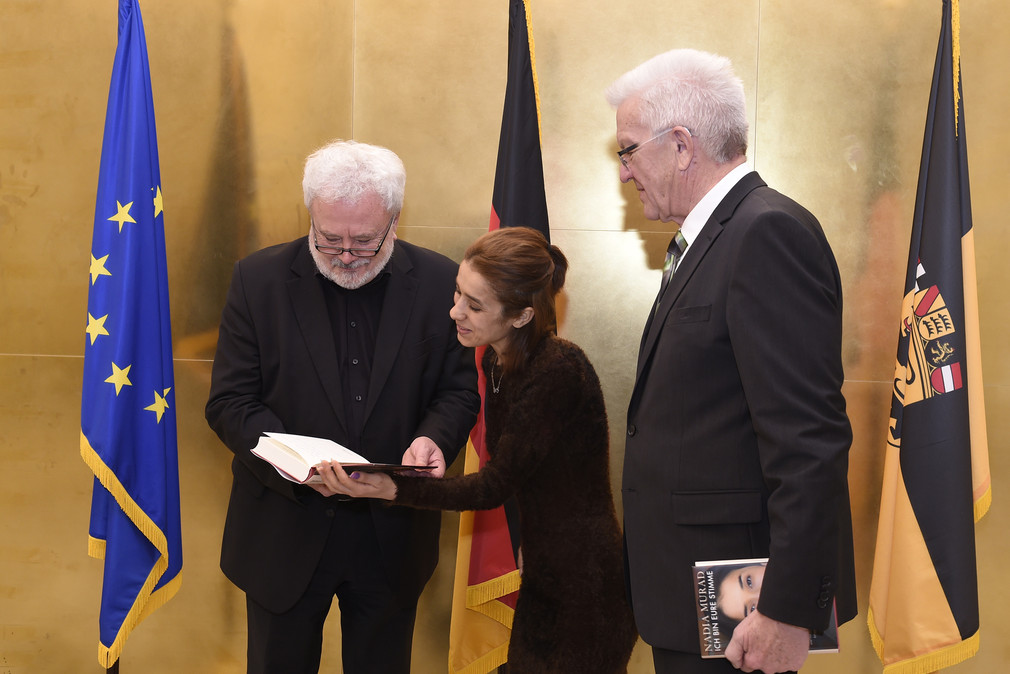Nadia Murad (M.) übergibt ihr neues Buch „Ich bin eure Stimme“ an Ministerpräsident Winfried Kretschmann (r.) und Staatsminister Klaus-Peter Murawski (l.)