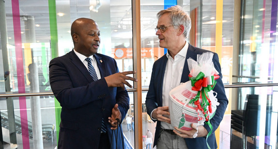 Der Botschafter der Republik Burundi und der Staatssekretär Rudi Hoogvliet stehen nebeneinander und schauen sich an. Sie haben sich gerade Geschenke überreicht und lächeln.