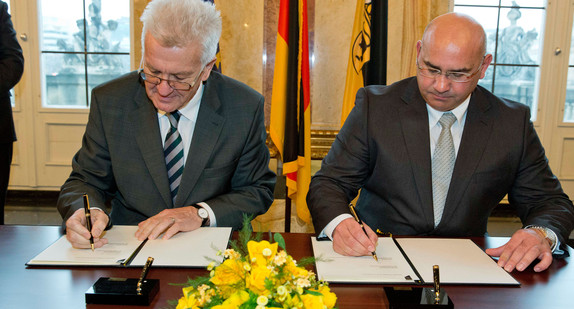 Ministerpräsident Winfried Kretschmann (l.) und Daniel Strauß (r.) unterzeichnen den Staatsvertrag