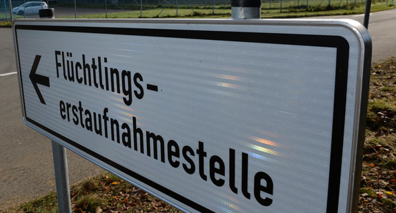Ein Schild mit der Aufschrift „Flüchtlingserstaufnahmestelle“, im Hintergrund ein Fahrzeug an einer Einfahrt.