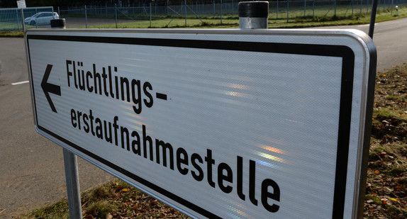 Ein Schild mit der Aufschrift „Flüchtlingserstaufnahmestelle“, im Hintergrund ein Fahrzeug an einer Einfahrt.