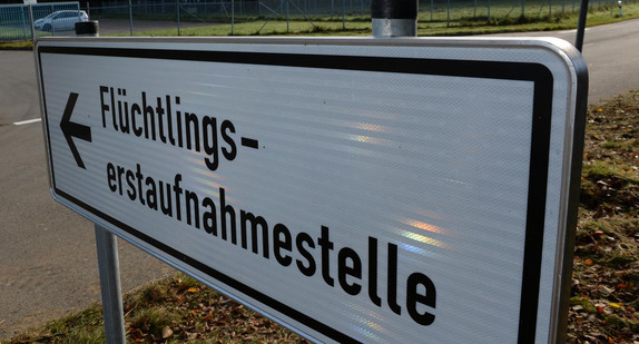 Ein Schild mit der Aufschrift „Flüchtlingserstaufnahmestelle“, im Hintergrund ein Fahrzeug an einer Einfahrt.