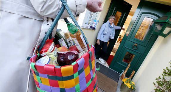 Eine Frau bringt ihrer Nachbarin Einkäufe. (Bild: © picture alliance/Roland Weihrauch/dpa)