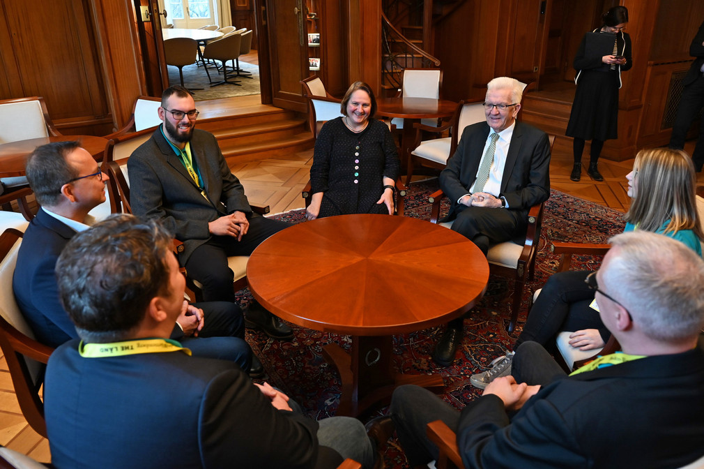 Eine Gruppe von Personen mit Ministerpräsident Winfried Kretschmann und Kultusministerin Theresa Schopper sitzt an einem runden Tisch.