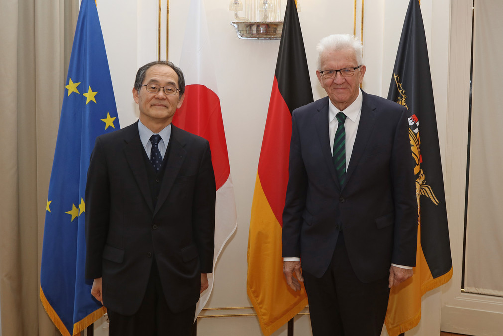 Ministerpräsident Winfried Kretschmann (rechts) und der japanische Botschafter Hidenao Yanagi (links) stehen in der Villa Reitzenstein vor Fahnen.