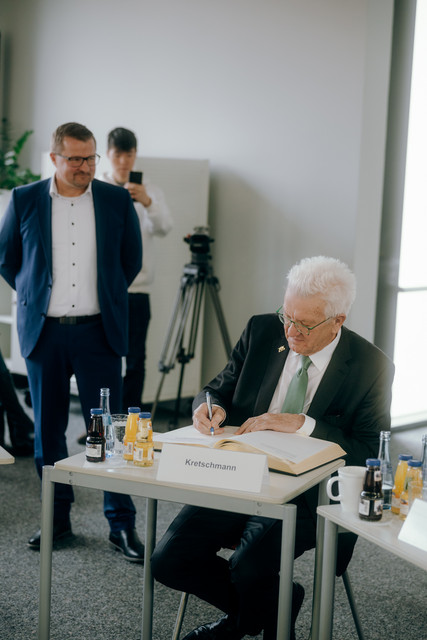 Pfullingens Bürgermeister Stefan Wörner (links, stehend) und Ministerpräsident Winfried Kretschmann (rechts, sitzend) beim Eintrag in das Gästebuch