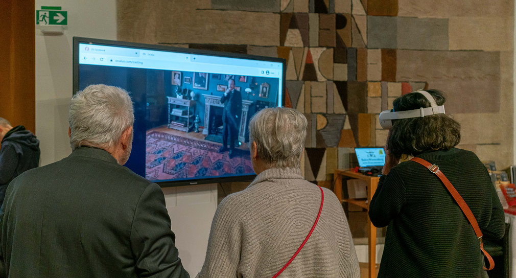 Gäste beim Betrachten einer Rekonstruktion der Wohnräume und der Kunstsammlung James Simons am Originalschauplatz via VR-Brille und Bildschilrm